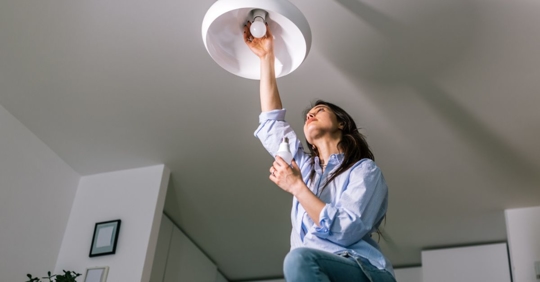 Young Woman Replacing Light Bulb in Chandelier